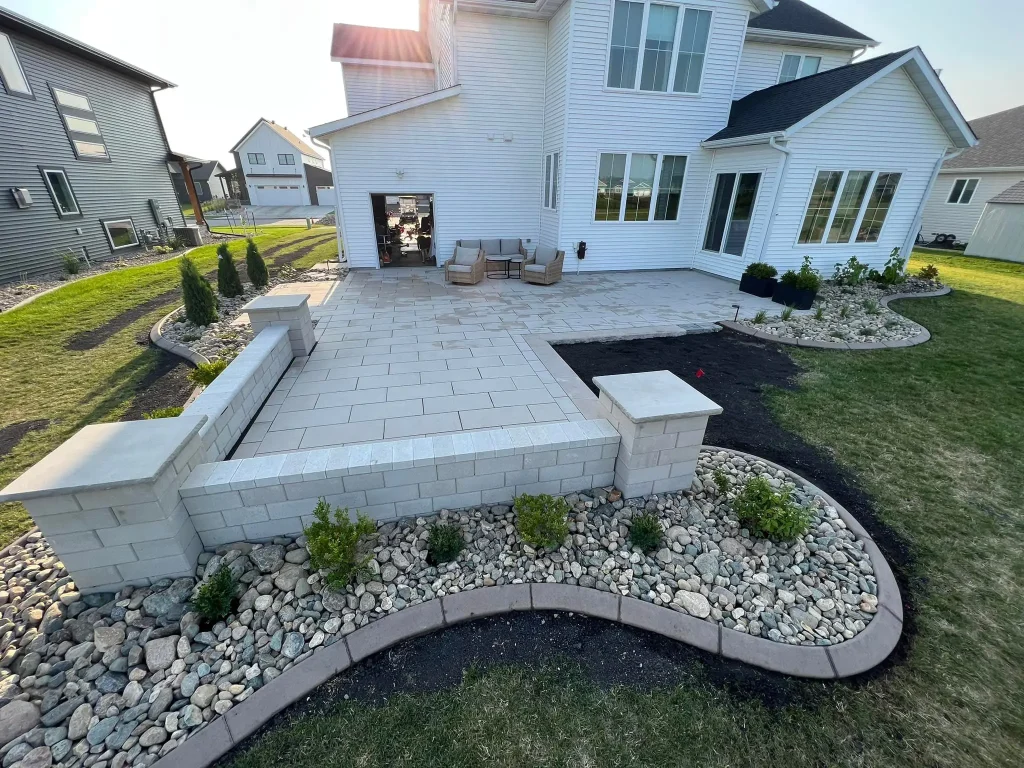 NicoleH-2 A modern backyard with a tiled patio and landscaped garden, adjacent to a white house.