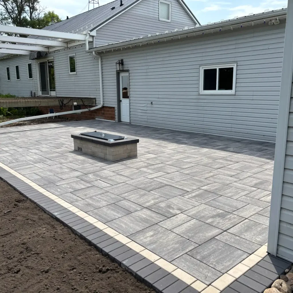 Patio_Fireplace0525-1 Newly installed gray tile patio with a central brick structure near a house with light gray siding.