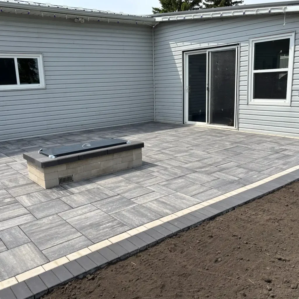 Patio_Fireplace0525-3 A gray paver patio with a rectangular brick structure, next to a building with a sliding glass door.