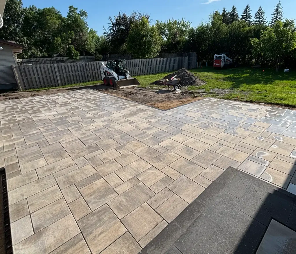 Patio1 A newly constructed patio with beige and brown tiles, next to a garden area with construction equipment.